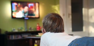 Kind liegt mit Fernbedienung in der Hand vor dem Fernseher