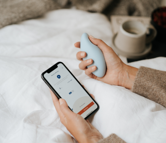 Atemtrainer in der einen, Smartphone in der anderen Hand. Das Gerät soll Schlafstörungen lindern