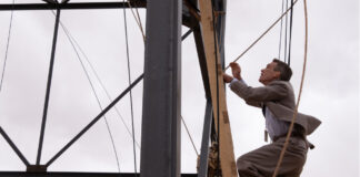 Szene aus "Oppenheimer": Cilian Murphy klettert an einem Turm hinauf