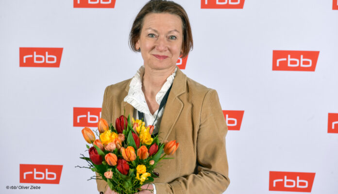 Martina Zöllner mit Blumenstrauß vor RBB-Wand