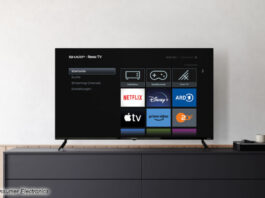 Ein Roku TV von Sharp in einem Beispielbild vor einer weißen Wand auf einem Sideboard