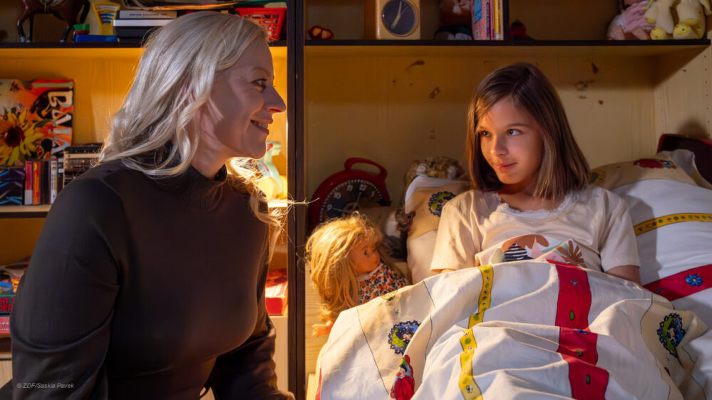 "Aktenzeichen XY... Ungelöst": Nachgestellte Szene: Nachts in einem Kinderzimmer liegt ein junges Mädchen wach in ihrem Bett und schaut liebevoll zu ihrer Mutter, die ihrer Blicke liebevoll und lächelnd erwidert.