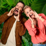 Dschungelcamp 2024: Jan Köppen und Sonja Zietlow stehen vor einer grünen Blätterwand und schreien belustigt in die Kamera.