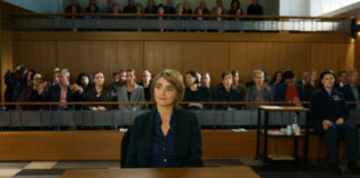 "Sie sagt. Er sagt.": Valerie Maiburg (Nicole Marischka) sitzt im Gerichtssaal im Zeugenstand und blickt zur Seite, hinter ihr sitzt das Publikum.