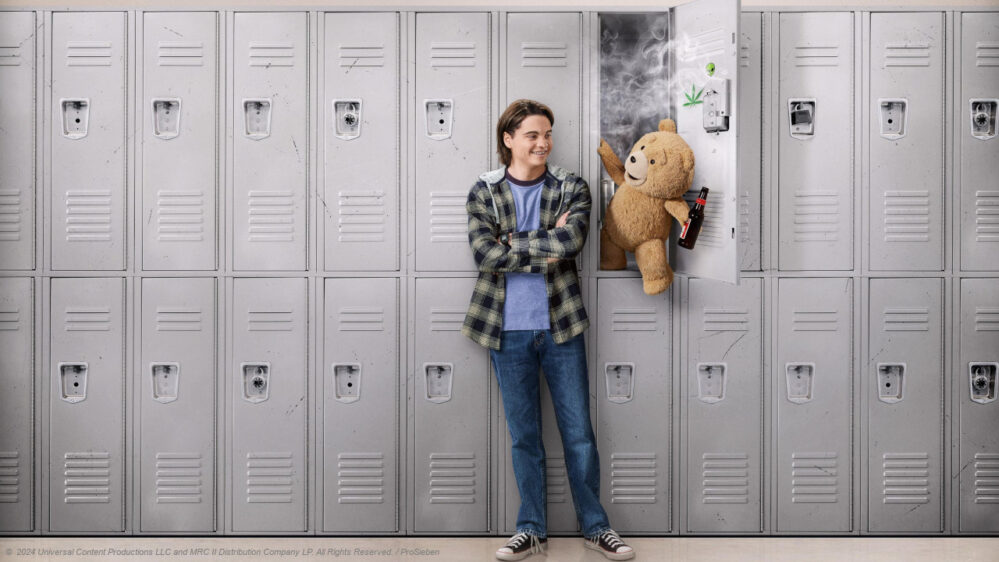 Teddybär Ted und sein Freund John an einem Spind in der Highschool. Ted hat eine Bierflasche in der Hand.