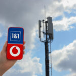 Smartphone mit Logos von Vodafone und 1&1 vor einem Funkmast