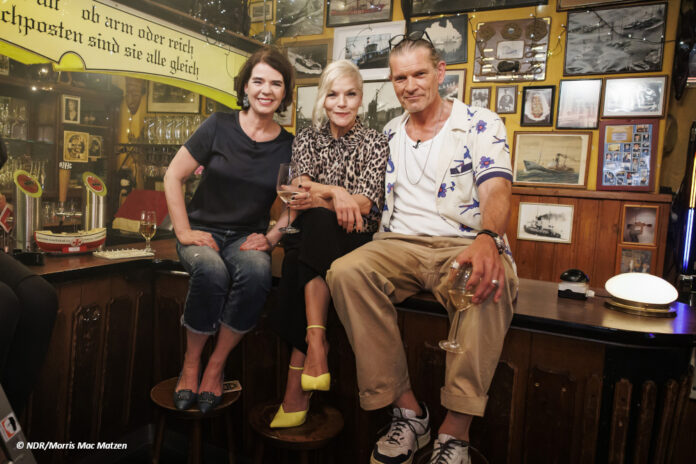 df_inas_nacht_200 Susanne Daubner, Ina Müller und Götz Otto sitzen auf einem Tisch in einer Kneipe und schauen in die Kamera