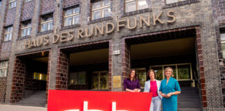 Die Geschäftsleitung des RBB steht vor dem Haus des Rundfunks und hält ein großes RBB-Schild vor sich