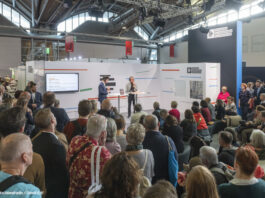 Ein Stand des Deutschlandradios auf der Frankfurter Buchmesse, Publikum hört einem stehenden Redner zu