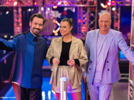 Jan Köppen, Laura Wontorra und Frank (Buschi) Buschmann stehen nebeneinander im Ninja-Warrior-Studio und lachen in die Kamera