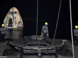 Drei Arbeitende bereiten den Abtransport des schwimmenden "Crew Drageon Endeavour" vor, das im Hintergrund im Meer schwimmt.