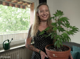 Eine Frau präsentiert eine Cannabis-Pflanze im Topf.