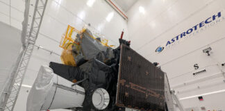 Ein Meteosat der dritten Generation steht auf einem Anhänger in einem Reinraum. Im Hintergrund stehen einige Menschen in Reinraumanzügen.