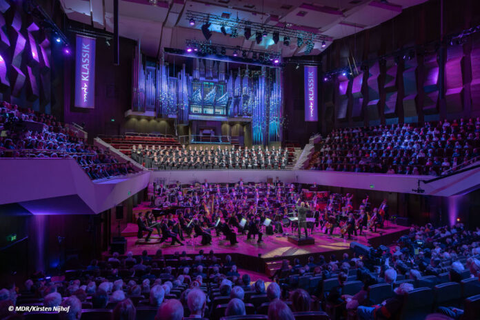 df_gewandhaus_bachfest_leipzig Ein Foto des vollen Gewandhauses Leipzig während eines Konzertes. Der Saal ist in bläuliches Licht getaucht und es hängen große Banner mit der Aufschrift "MDR Klassik" im Raum.