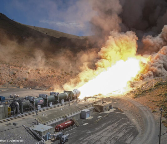 Ein horizontal am Boden montiertes Raketentriebwerk wird getestet. Aus der Rakete tritt ein in Richtung eines Hügels gerichteter, großer Feuerball aus.