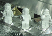 Drei weiße Legofiguren stehen auf einem mit Aluminiumfolie verkleideten Objekt.
