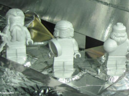 Drei weiße Legofiguren stehen auf einem mit Aluminiumfolie verkleideten Objekt.