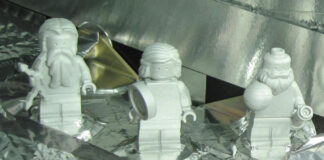 Drei weiße Legofiguren stehen auf einem mit Aluminiumfolie verkleideten Objekt.