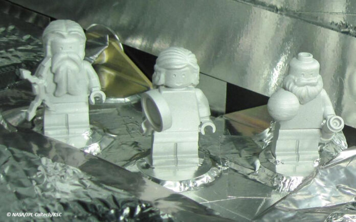 df_juno_lego Drei weiße Legofiguren stehen auf einem mit Aluminiumfolie verkleideten Objekt.