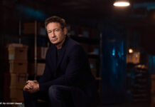 Der Schauspieler David Duchovny sitzt in einem abgedunkelten Raum und schaut in die Kamera.