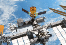 Ein Renderbild zeigt die Internationalen Raumstation mit einem angedockten "HTV-X"- Raumfrachter von "oben". Im Hintergrund sieht man das Blau der Erde und ein paar Wolken.