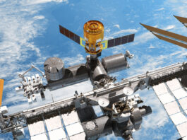 Ein Renderbild zeigt die Internationalen Raumstation mit einem angedockten "HTV-X"- Raumfrachter von "oben". Im Hintergrund sieht man das Blau der Erde und ein paar Wolken.