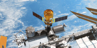 Ein Renderbild zeigt die Internationalen Raumstation mit einem angedockten "HTV-X"- Raumfrachter von "oben". Im Hintergrund sieht man das Blau der Erde und ein paar Wolken.